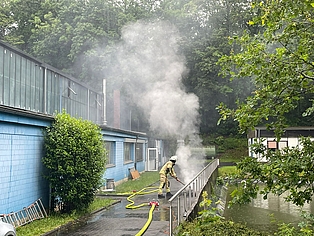 Feuerwehrmann löscht rauchende Teile neben einer Firma